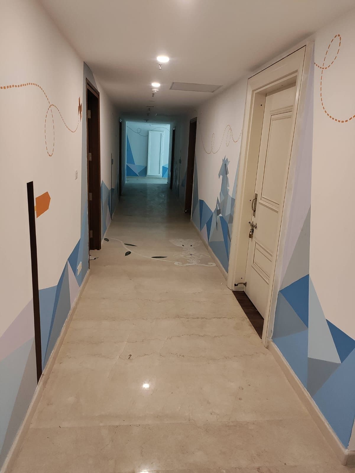 Corridor in a Chennai commercial building, finished with blue geometric wall graphics and a dashed line motif, doors either side and recessed ceiling lights.