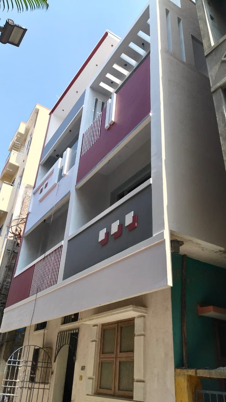 Completed three-storey house in Chennai seen from the street, faced in maroon and grey panels with vertical fin louvres screening the balconies.