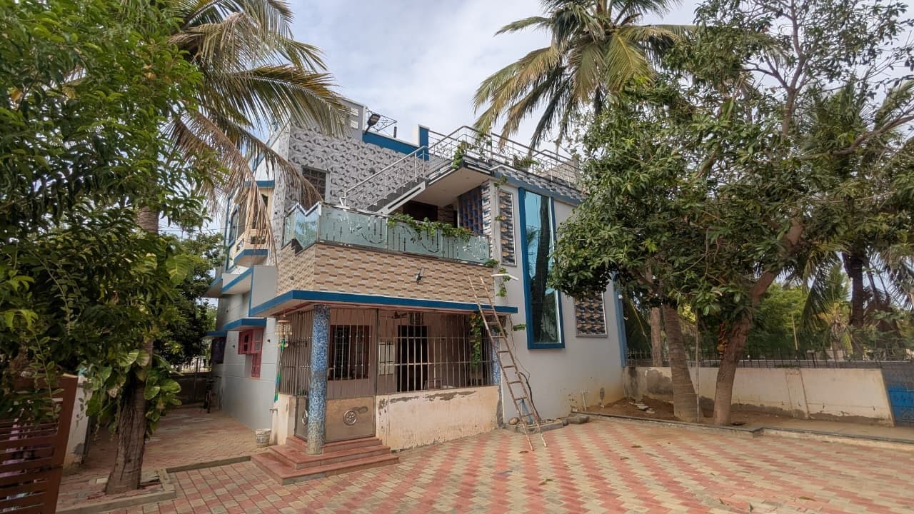 Completed two-storey residence finished in grey and blue render with textured cladding tile, an etched-glass balcony railing and an external stair rising to the roof terrace, seen across a paved forecourt.