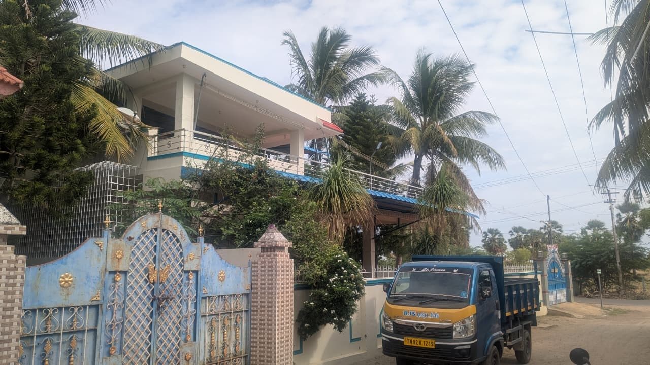 Completed two-storey residence seen from the road, finished in white with teal banding, a blue profiled canopy over the terrace and an ornamental gate, with an RJS Construction tipper parked at the kerb.