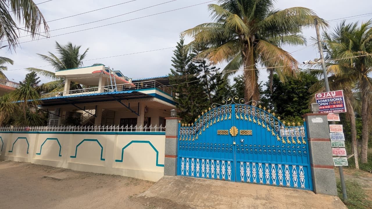 The same residence from the front, showing the full-width terrace under its canopy behind a cream compound wall carrying a painted teal geometric band.