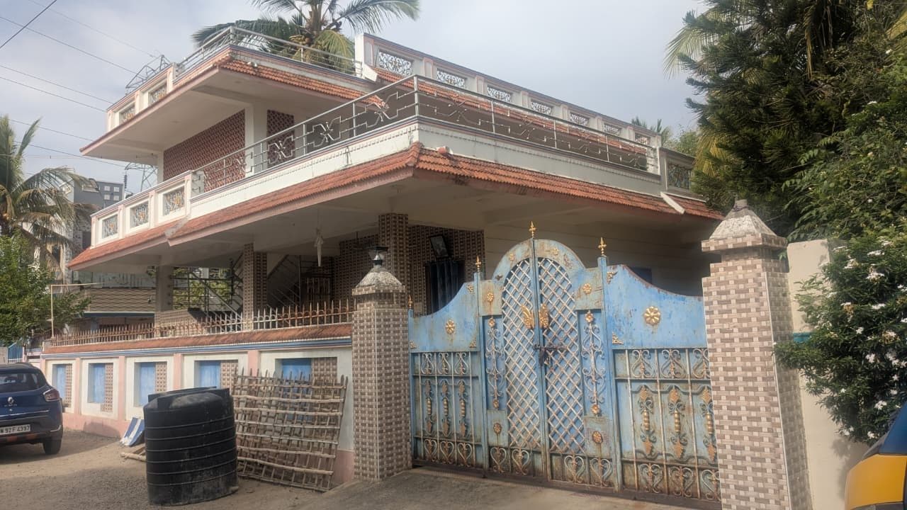 Frontage of the same residence showing the tiled sunshade over the entrance, the jaali parapet panels and the ornamental gate between rendered piers.