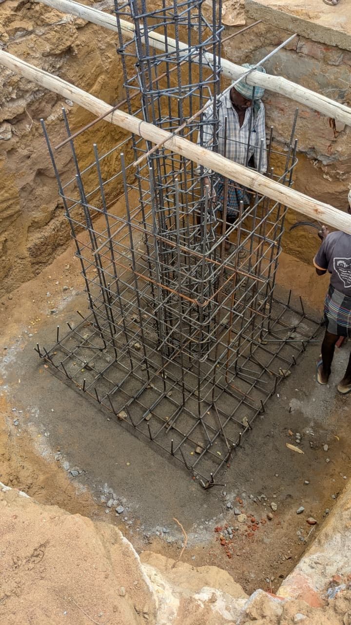 Two site workers tying the lateral reinforcement of a column cage inside the excavated footing pit.